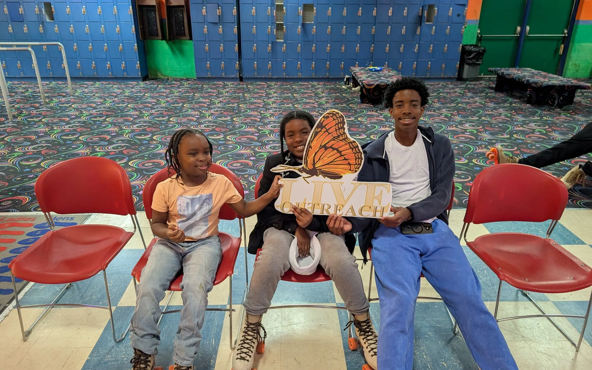 Three young people smiling at a roller skating rink holding the L.I.V.E. Outreach butterfly sign