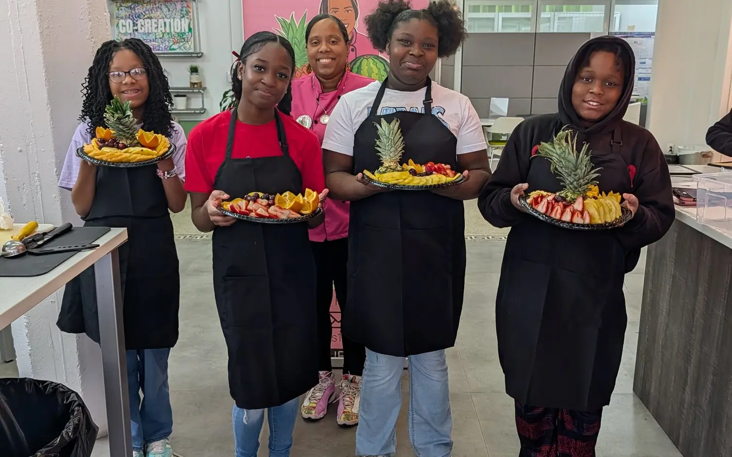 Youth in aprons proudly holding fruit platters they made during a L.I.V.E. Outreach cooking workshop