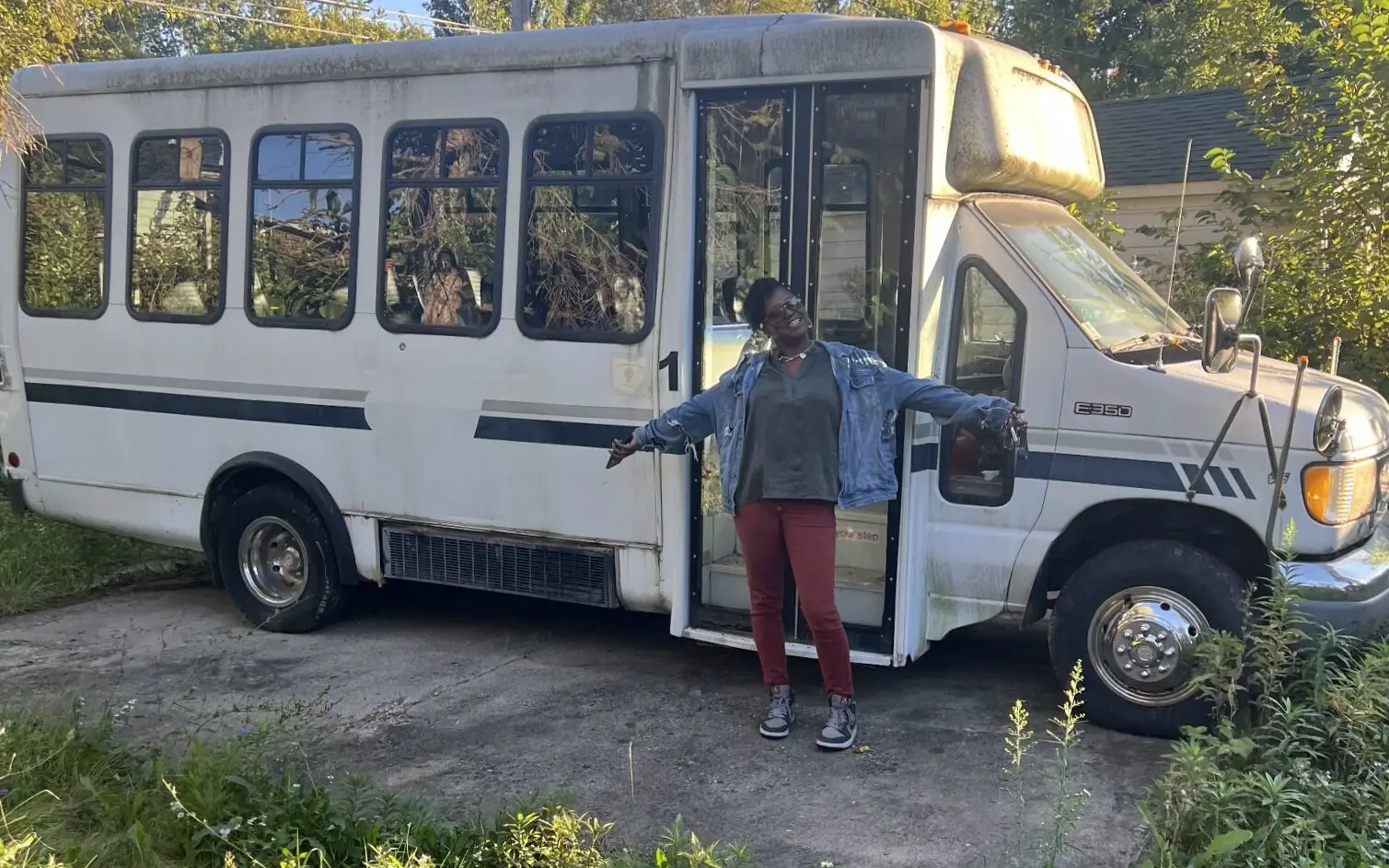 A woman stands with arms outstretched in front of the Mobile Mentoring Hub bus with its doors open